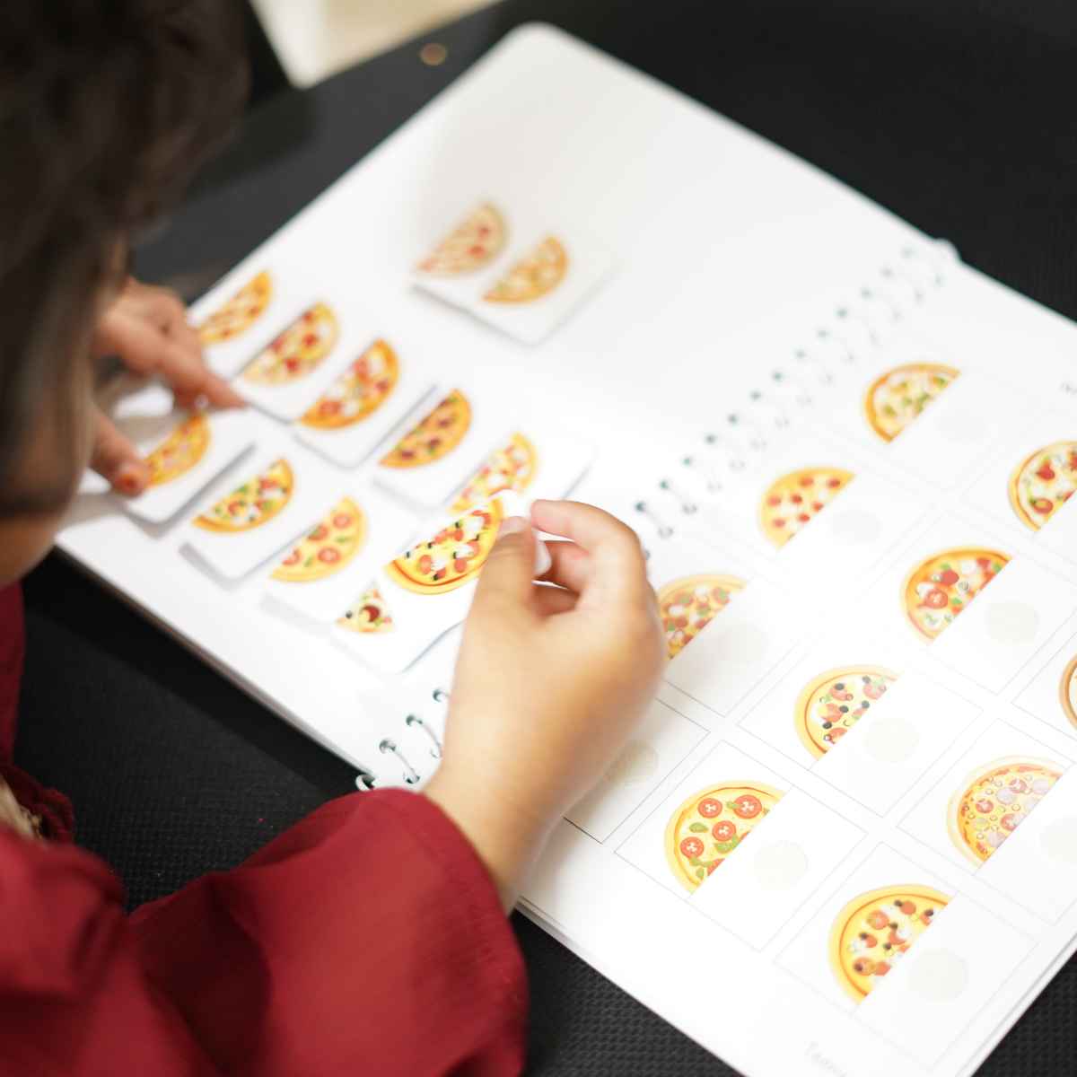 Child playing with a learning activity book featuring pizza illustrations